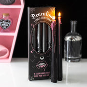 Set of pink-drip vampire taper candles burning next to gothic-themed packaging on a white surface with Halloween decor in background.
