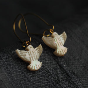 A pair of Pearl Dove Bird Earrings with gold-plated ear wires on a dark background.