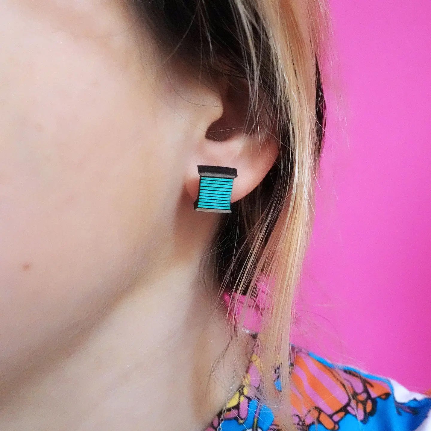 Turquoise bobbin thread earring worn on ear – laser-cut sustainable wood stud for crafters and sewing enthusiasts.