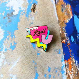 Silly Loaf Retro 80s Enamel Pin on a distressed blue and wooden background, featuring a geometric design with ‘Rad!’ lettering.