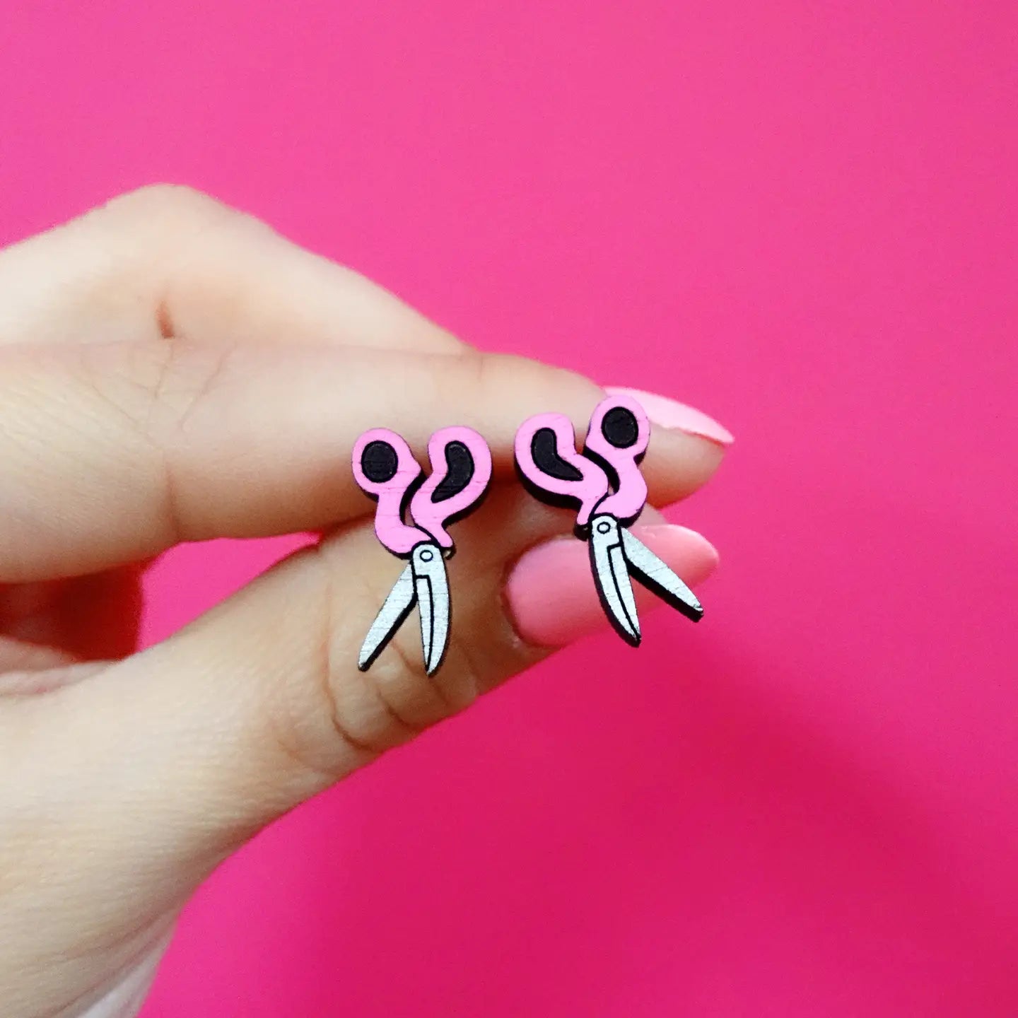 Front view of pink scissors stud earrings on hand – novelty sewing jewellery.