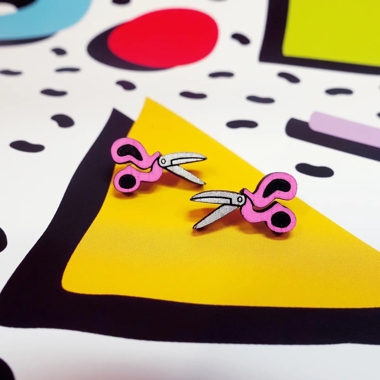Flat lay of scissors earrings on colourful patterned background – quirky stud jewellery.