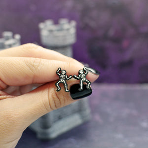 Close-up of Silly Loaf Skeleton Stud Earrings held by a hand with black nails.