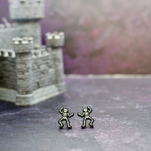 Silly Loaf Skeleton Stud Earrings displayed against a purple castle backdrop.