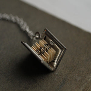 A close-up of the silver book locket, fully open, displaying tiny printed pages inside.