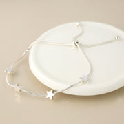 Silver plated snake chain bracelet with five star charms laid on a white ceramic plate.