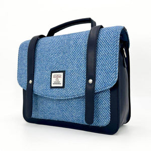 Angled view of sky blue Harris Tweed messenger bag showing flap closure, top handle and structured shape.