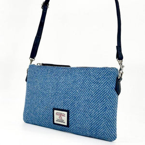 Sky blue Harris Tweed zip bag worn as a shoulder bag with adjustable navy strap and silver hardware.