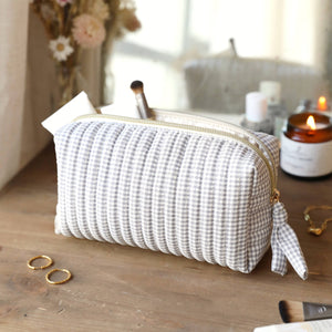Small grey gingham linen travel bag with gold zip on wooden vanity beside candle and jewellery.