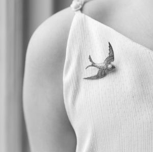 A black and white image of a person wearing the swallow brooch on a light-coloured outfit, pinned near the shoulder.