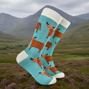 Fluffy Wee Hairy Coo Socks in duck egg blue on Highland landscape background