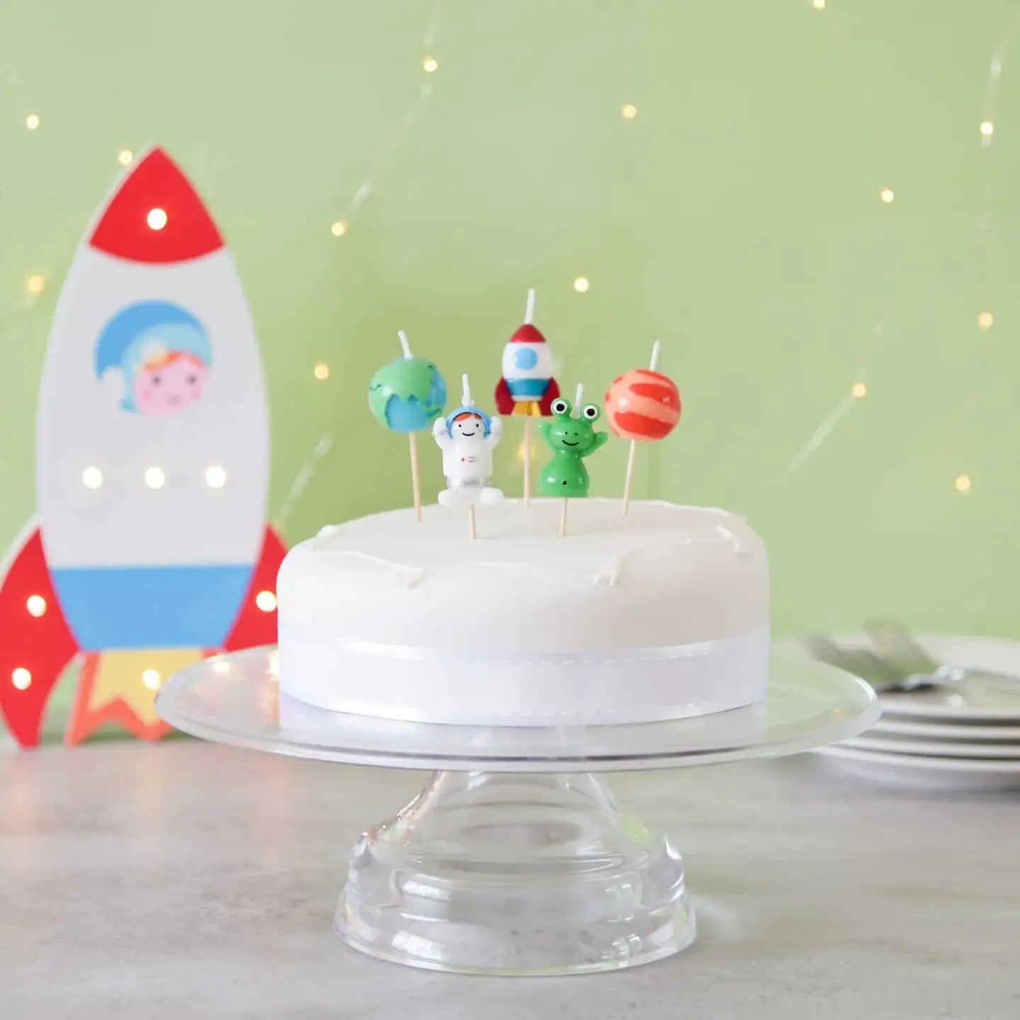 Space-themed cake with 3D rocket, alien and planet candles on top – fun birthday cake decor.