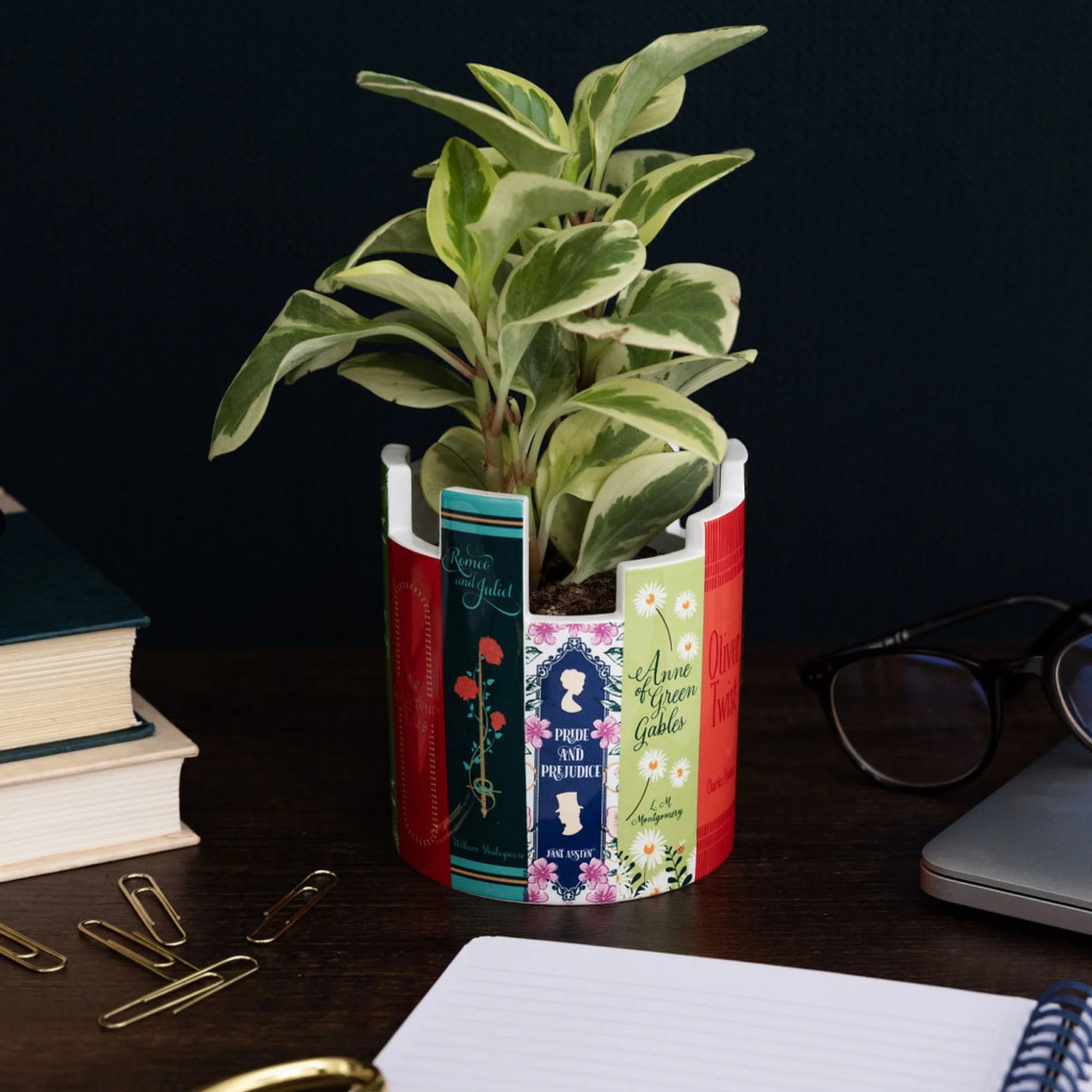 Book-themed ceramic pot with a plant inside, styled on a desk beside glasses, gold stationery, and open notebooks for a literary workspace vibe.
