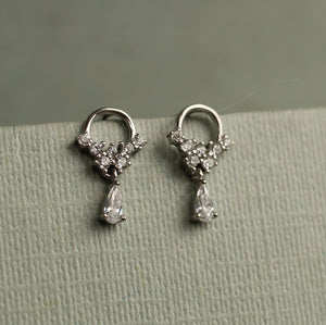Detailed view of sterling silver crystal mini hoop earrings with cluster of round cubic zirconia stones and dangling teardrop crystal, set against textured green card.
