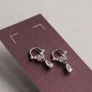 Side angle of sterling silver crystal droplet hoop stud earrings, featuring a sparkling cluster of cubic zirconia and pear-shaped drop, presented on plum-coloured display card.