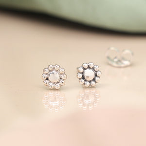 Tiny sterling silver floral stud earrings with butterfly backs on soft cream surface.