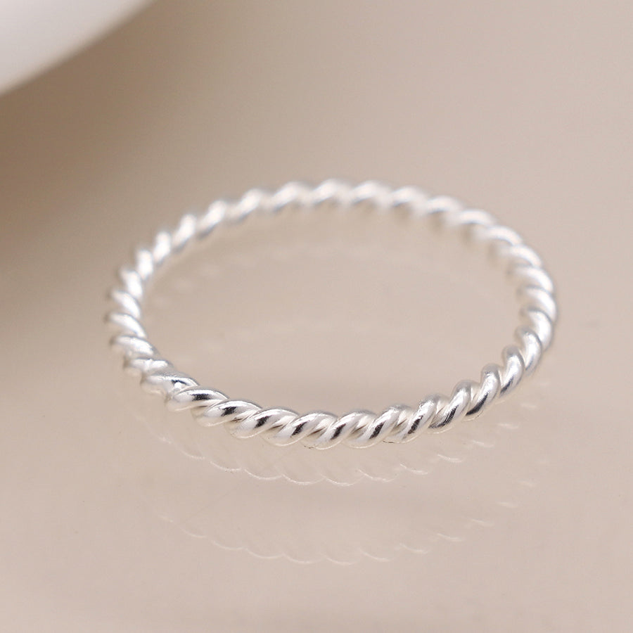 Sterling silver simple twist ring on reflective surface.