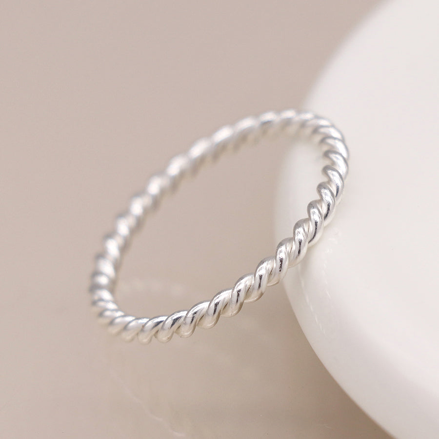 Side view of twisted silver ring leaning on white dish.