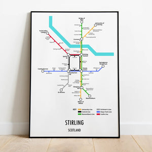 A framed Underground-style transport map print of Stirling, Scotland, featuring key city locations in a modern design, placed on a wooden floor against a white wall.