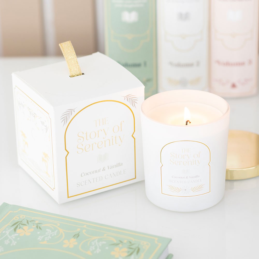 The Story of Serenity Coconut & Vanilla Candle lit in frosted white jar with gold lid, shown beside elegant illustrated gift box.