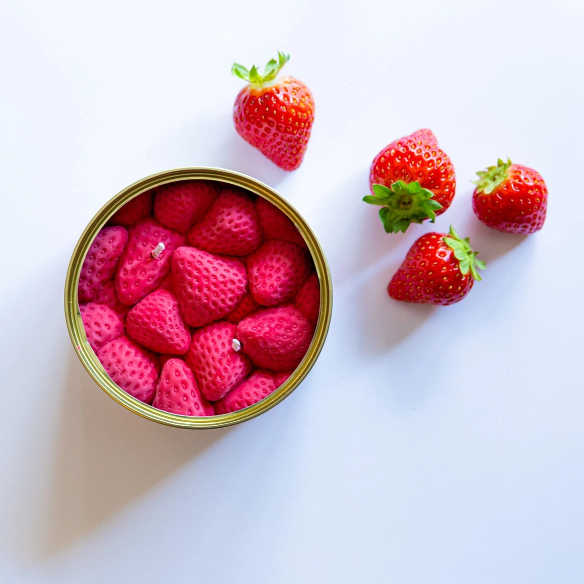 Strawberry Scented Tin Candle displayed next to real fresh strawberries on a white background, highlighting the candle’s realistic design.