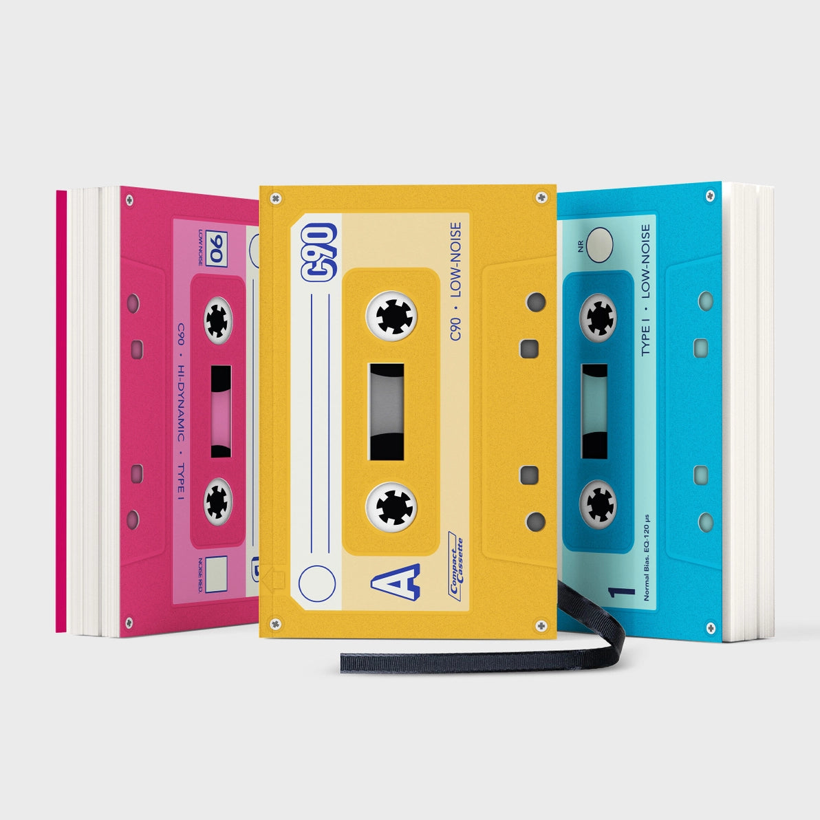 Three colourful cassette-style notebooks in pink, yellow, and blue, standing upright and designed to look like retro mixtapes.