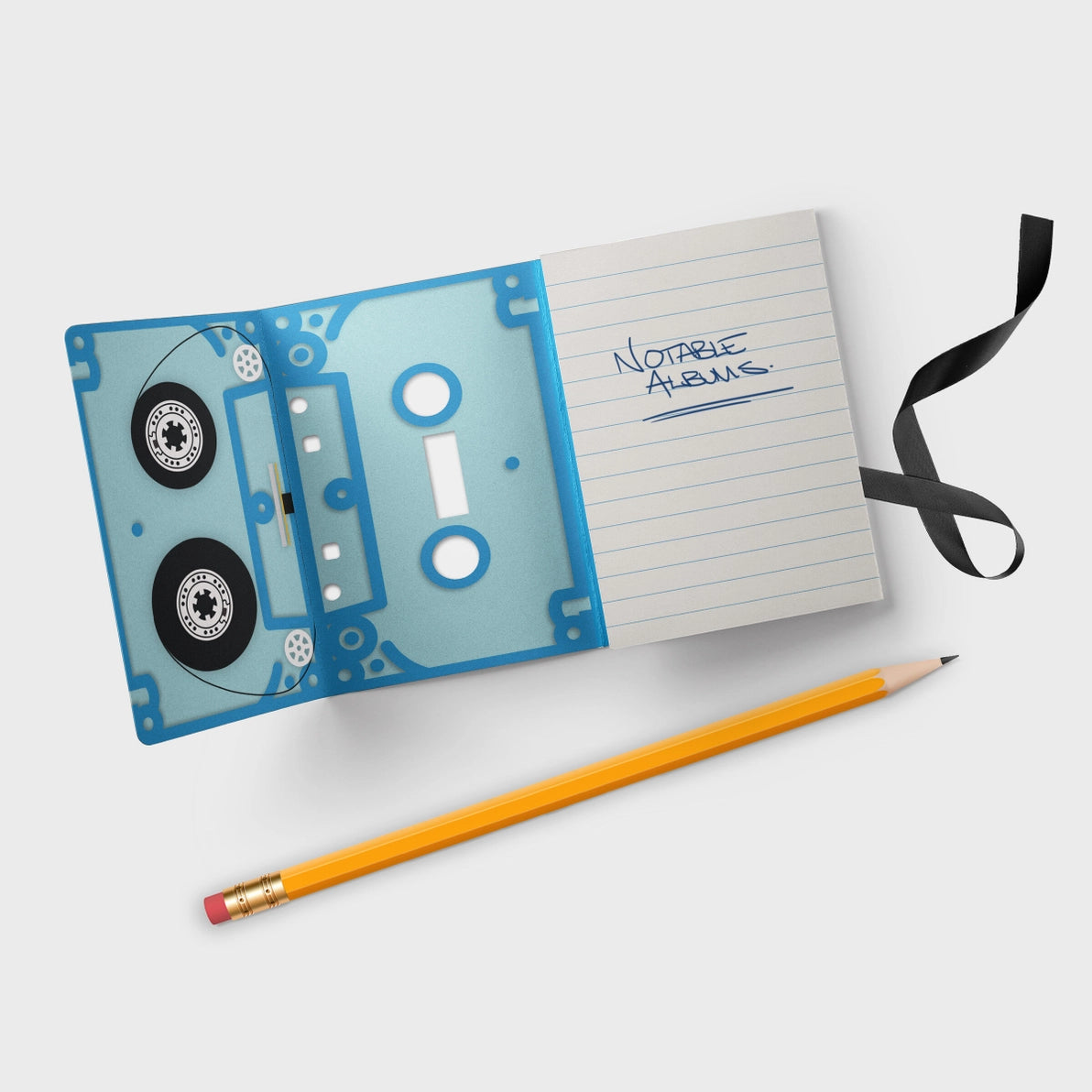 Flat-lay of an open blue Mixtape Notebook styled like a cassette tape, with pencil and black ribbon bookmark