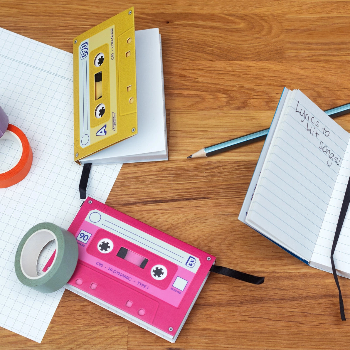 Mixtape Notebooks on a wooden desk surrounded by stationery, used for writing lyrics and notes, with tape-style designs