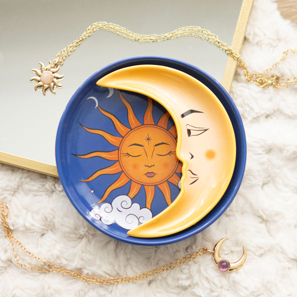Sun and Moon ceramic stacking trinket dish with golden crescent moon resting on blue sun tray, surrounded by celestial-themed jewellery on soft fabric.