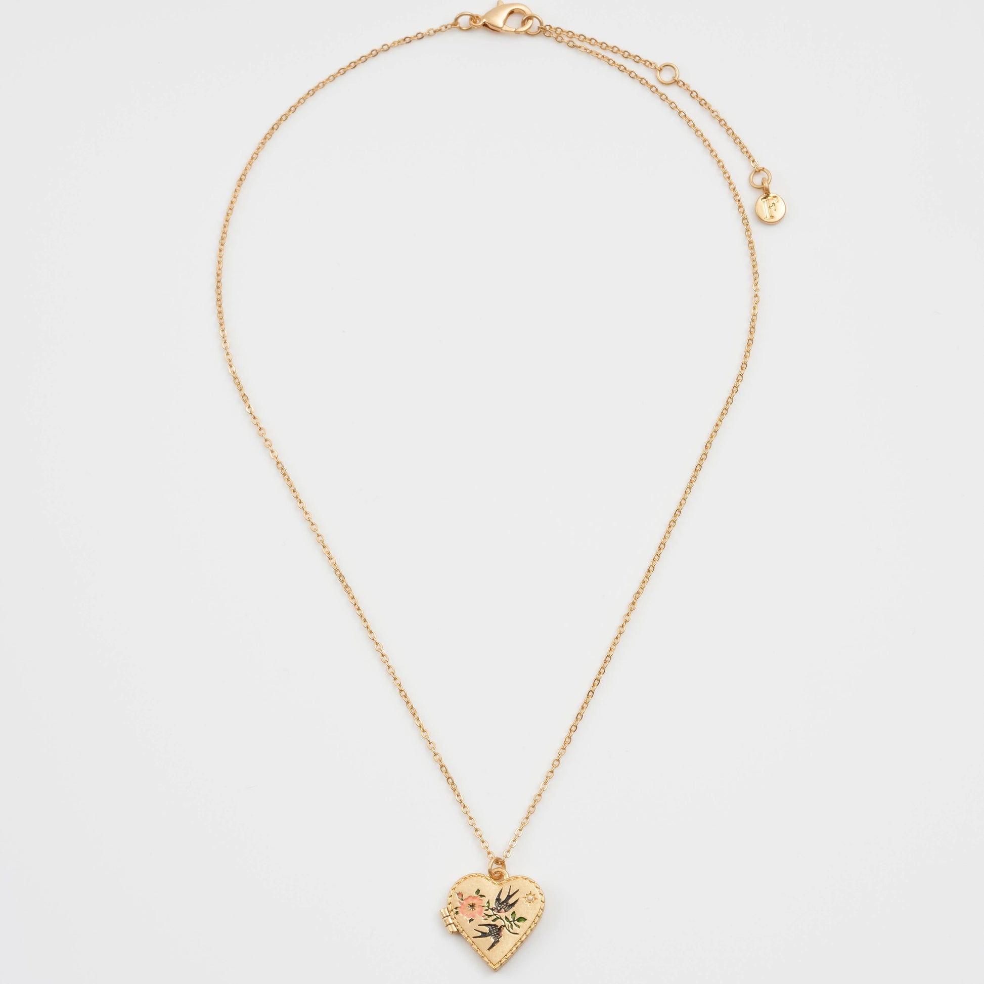 Full view of gold-plated swallow heart locket necklace laid flat, showing delicate chain and small heart pendant with floral enamel detail.