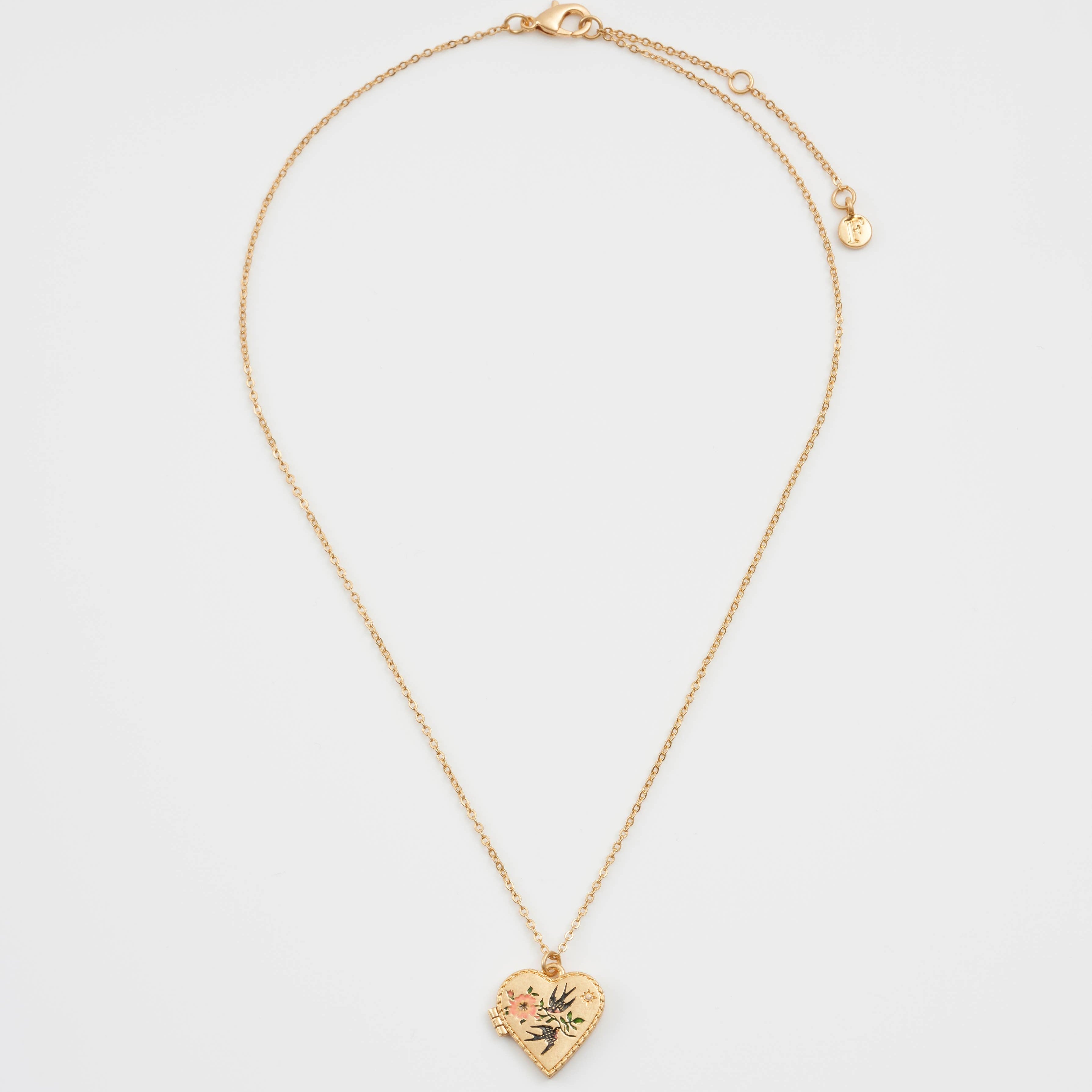 Full view of gold-plated swallow heart locket necklace laid flat, showing delicate chain and small heart pendant with floral enamel detail.
