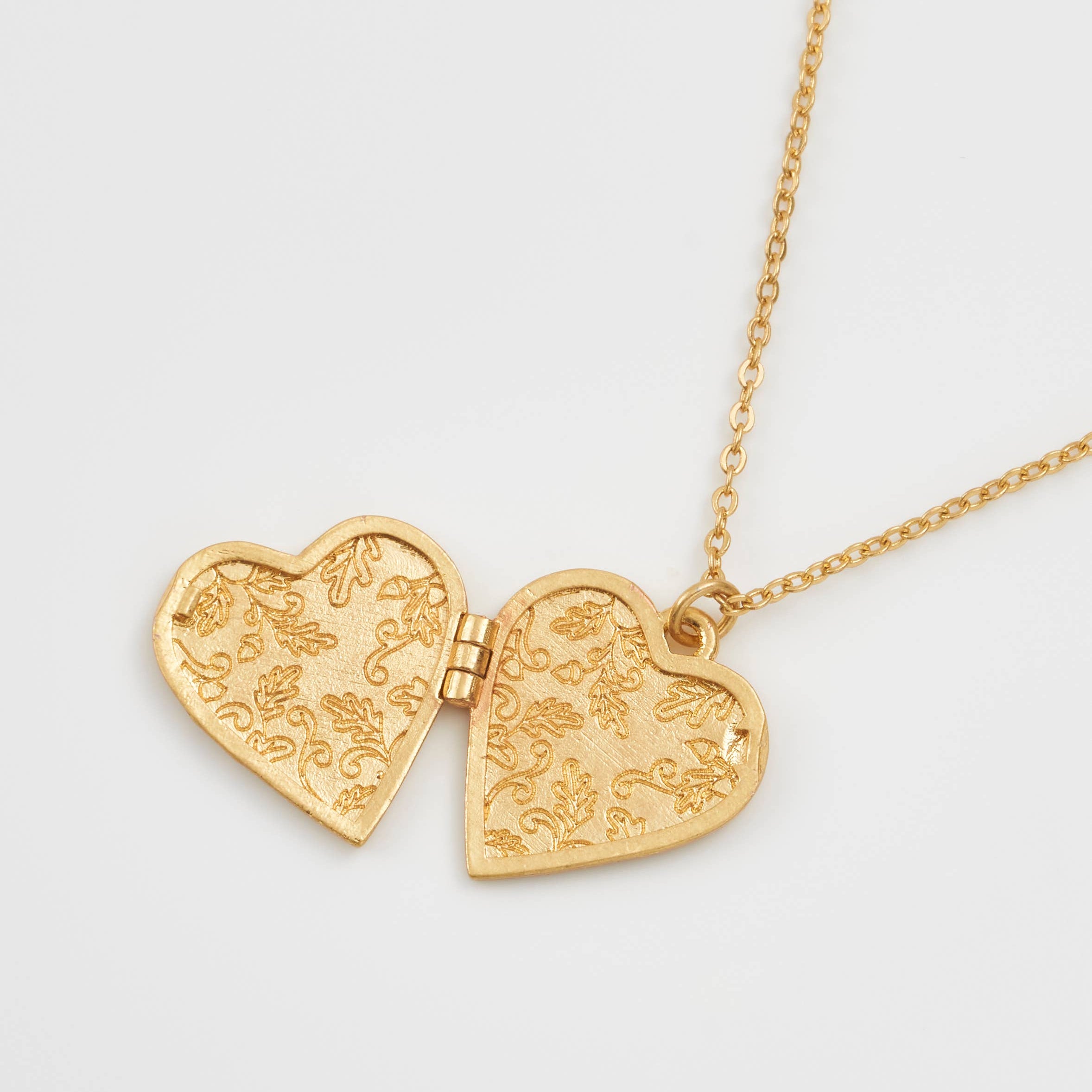Open gold-plated heart locket showing engraved floral interior pattern with delicate detailing on both sides.
