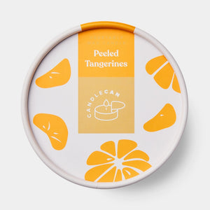 Tangerine-scented candle in an open tin being lit with a match, styled on a tray with home décor accessories for a cosy interior vibe.