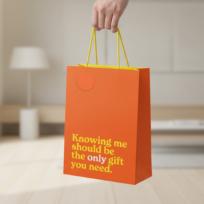 Orange medium gift bag with yellow slogan held by hand in room setting