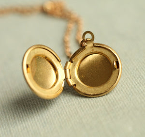 Open Tiny Brass Dandelion Locket showing space for two photos, with a blurred gold chain in the background.