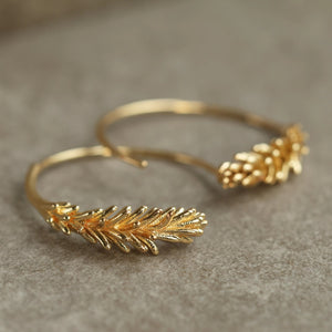 A close-up shot of the Tiny Gold Leaf Hoop Earrings against a neutral stone background, showing their shimmering gold finish.