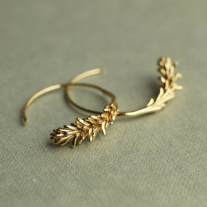 A pair of Tiny Gold Leaf Hoop Earrings lying on a textured surface, displaying the graceful curvature and leaf-inspired detailing.