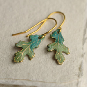 Pair of handmade Tiny Oak Leaf Earrings with intricate veining details, laid on textured paper.