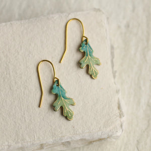 Delicate turquoise oak leaf earrings with gold-plated hooks, photographed on a soft cream surface.