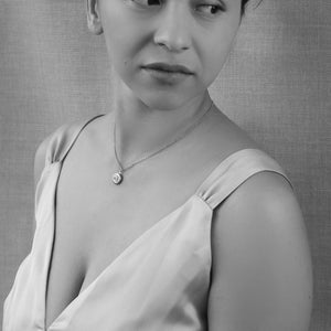 Woman wearing a tiny silver daisy locket necklace on a fine chain – minimalist floral jewellery styled with a satin dress.