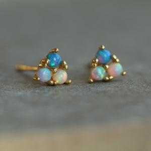 Angled view of opal stud earrings on a textured surface, highlighting the depth of colour and gold-plated silver claw setting.