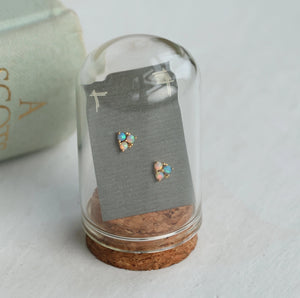 Turquoise trio opal stud earrings presented in a glass dome display with a cork base, showing off their luminous shimmer.