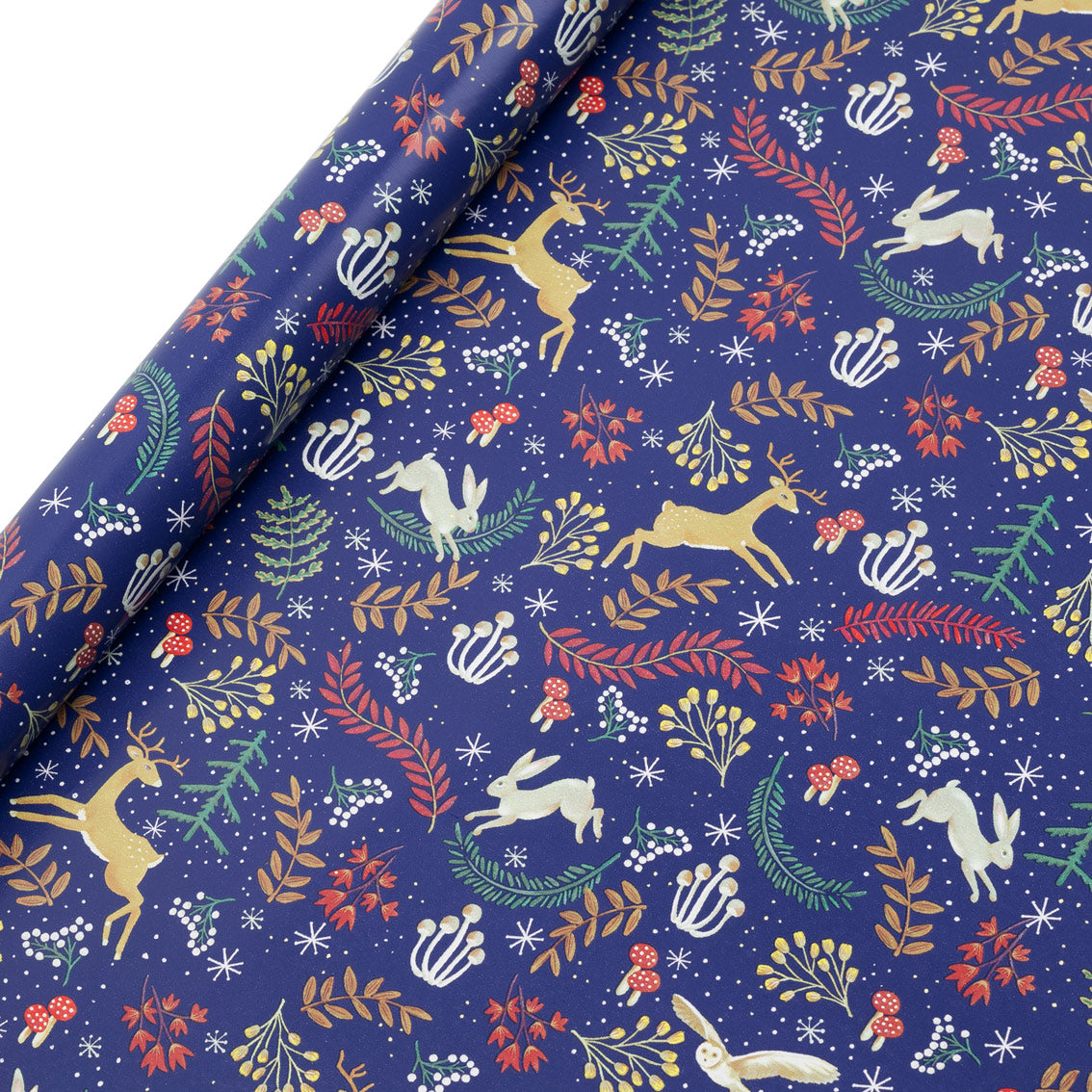 Festive recycled Christmas wrapping paper with woodland animals and jewel-tone florals on navy blue background, shown partially unrolled.
