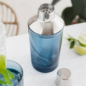 Open twist glass cocktail shaker with strainer visible, surrounded by lime and mint – functional and elegant barware.