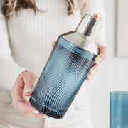 Person holding a blue twisted glass cocktail shaker with stainless steel top – stylish home bar essential