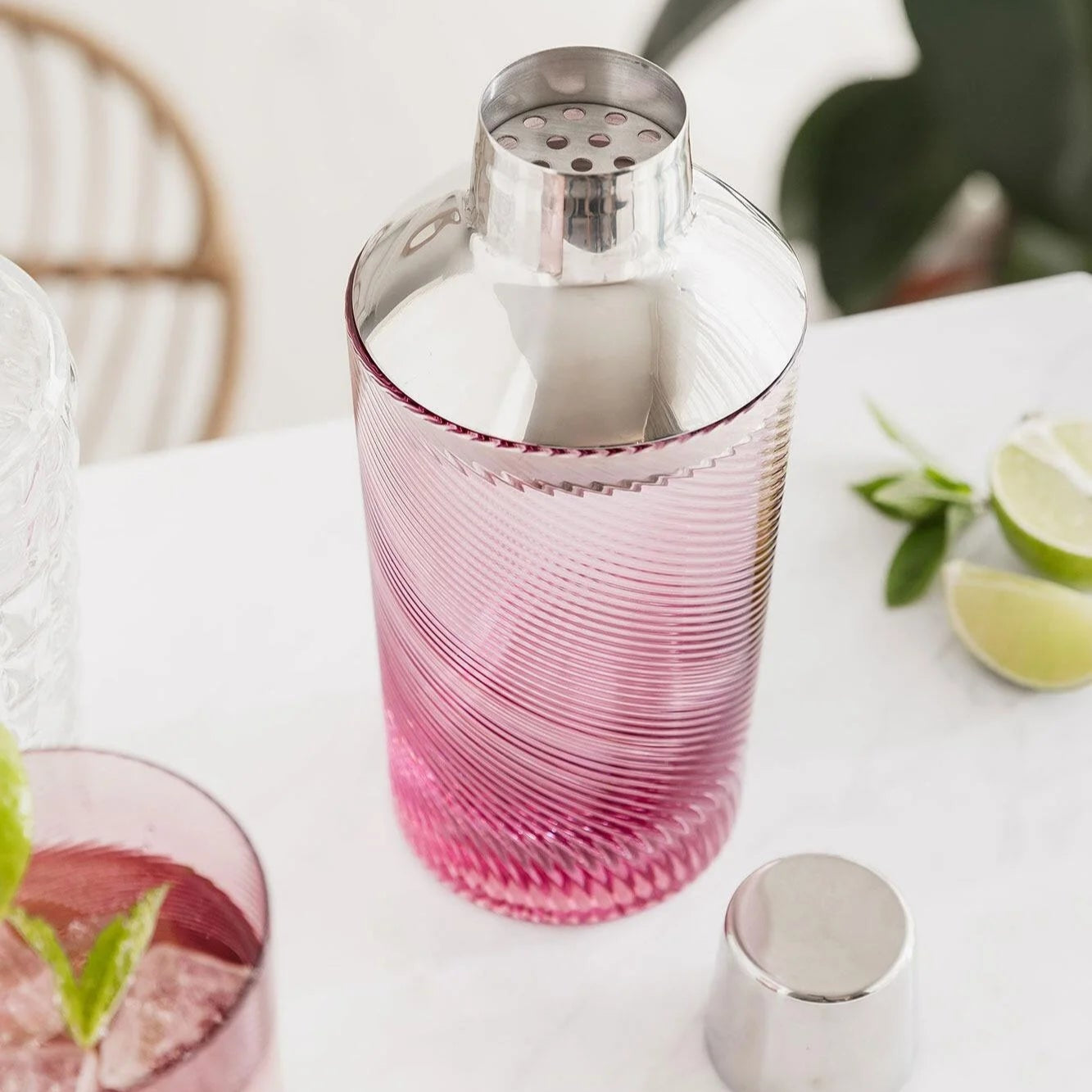 Open pink twist cocktail shaker with strainer exposed, styled with lime wedges and mint on a bright surface.