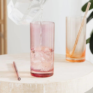 Water being poured into pink twist highball tumbler beside peach glass.