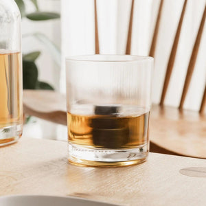 Whisky served in twist spinning glass with granite stones on light wooden table.