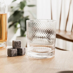 Empty twist whisky glass with granite whisky stones beside it on wooden table.