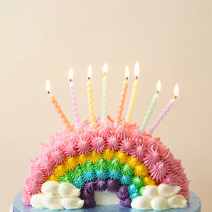 Pastel spiral birthday candles on a rainbow frosting cake ready to celebrate.